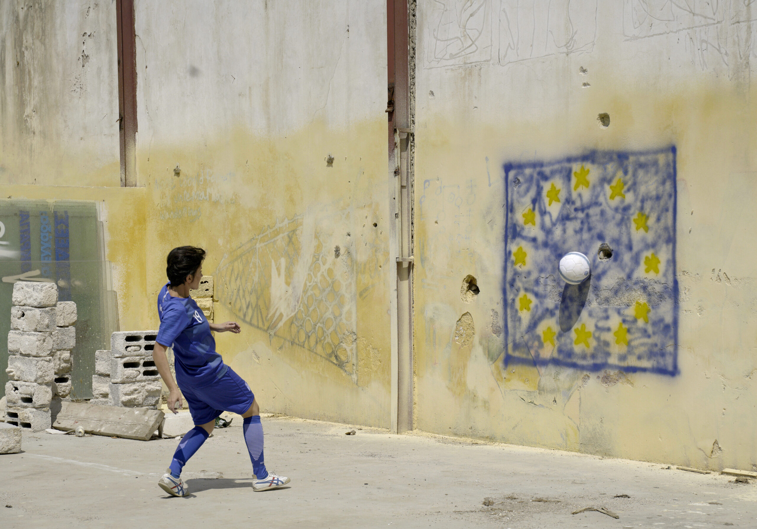 Sokratis, palla al centro, Produzione on the Breadline, video 4K, 5’ 10”, colori foto su carta Hahnemülhe, 80x100 cm, 2019